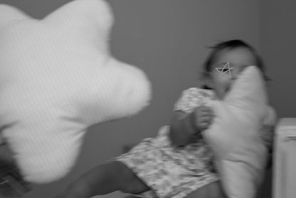 A black and white photo of a baby sitting and holding a large star pillow, with another star pillow blurred in the foreground.